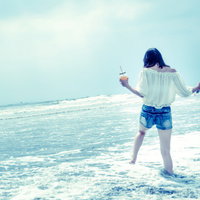 浅瀬の波打ち際ではしゃぐ若い女性の後ろ姿の写真