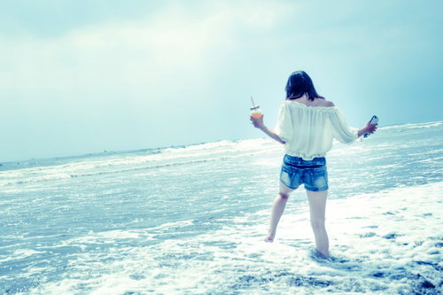 浅瀬の波打ち際ではしゃぐ若い女性の後ろ姿