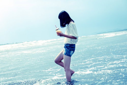裸足で波打ち際に立つガーリーな女性のビーチ