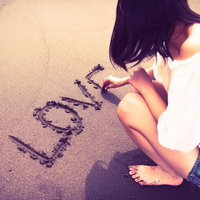 砂浜にLOVEと文字を書く女性のうしろ姿の写真