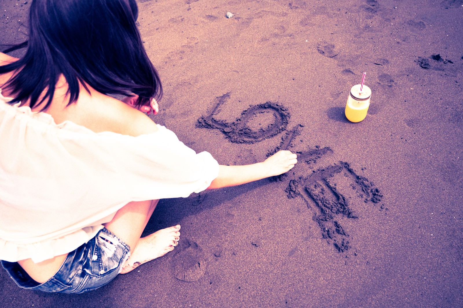 砂浜に指でLOVEの文字を書いている白いトップスの女性