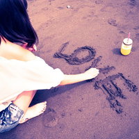 砂浜にLOVEの文字を書く白いトップスの女性の写真