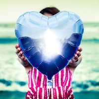 青色のハート型風船を差し出すストライプシャツの女性の写真