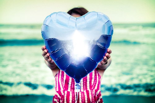 青色のハート型風船を差し出すストライプシャツの女性