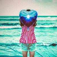 ビーチでハート型の風船を掲げる女性の写真