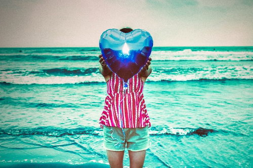 ビーチでハート型の風船を掲げる女性