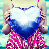 海を背景にピンクの衣装でハートを持った女性の写真