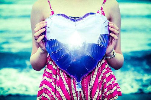 海を背景にピンクの衣装でハートを持った女性