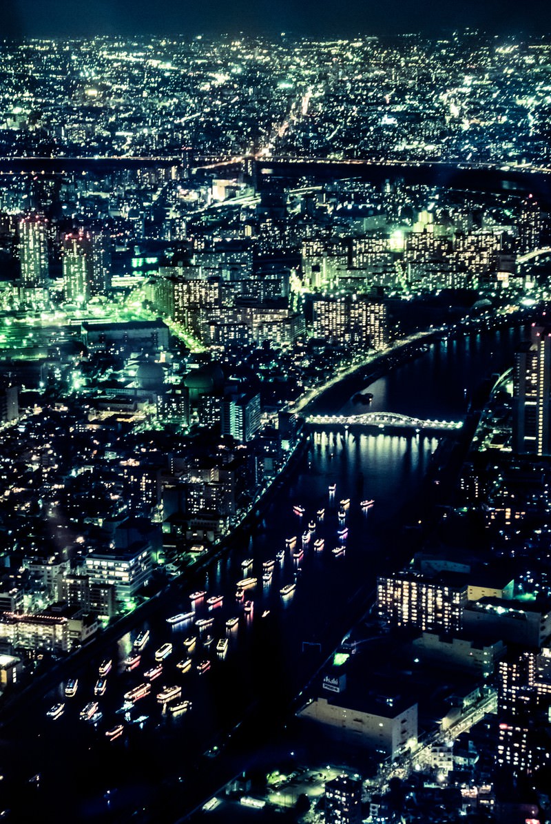 高層ビル群の夜景を背景に、ライトアップされた屋形船が川を進む様子