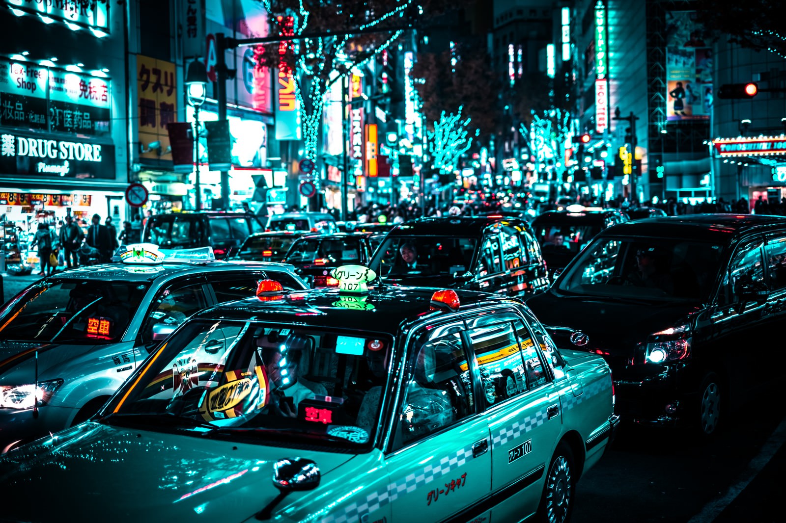 渋谷駅前の夜、ネオンが光る中で赤信号待ちをするタクシーの列