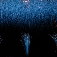 夜空を彩る青い光、降り注ぐ打上げ花火、夏の夜間イベントの写真