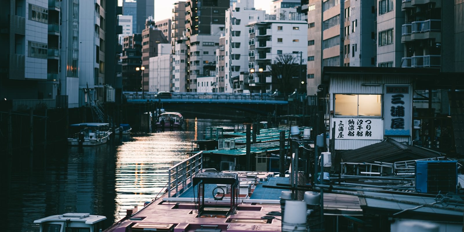 夕暮れの神田川に停泊する釣り船と屋形船、背景に高層マンション