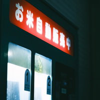 恍惚と点灯したお米自動販売機の照明と商品展示の写真