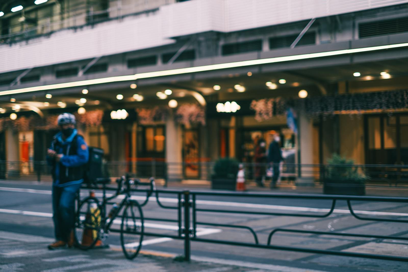 歩道で自転車を降りて立つ配達員の街角の風景