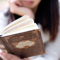 洋書を片手に読み進める女性の学習風景の写真