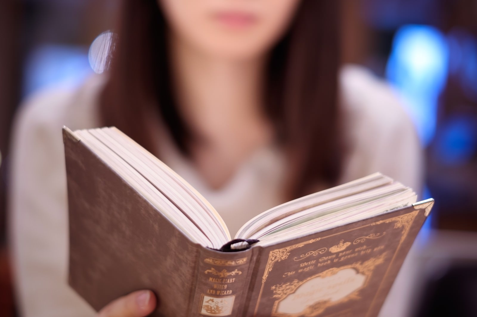 カフェで洋書を読む女性の手元と上半身