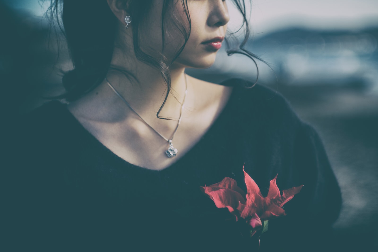 暗い背景で俯く女性、胸元に小さな赤い花