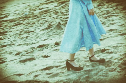 2人で行った旅行先の海岸を歩く女性の足元