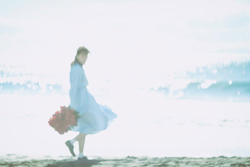 海面の反射と彼女が歩く波打ち際の夏のデート風景