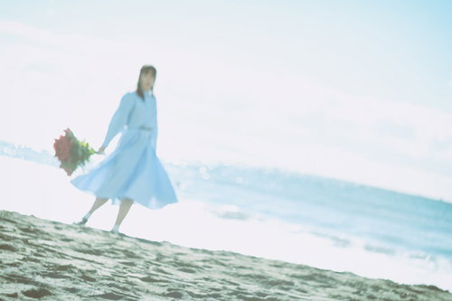 爽やかな朝の海辺で白いワンピースを着た女性が花束を持つ