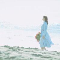 陽の光と海風を感じながら波打ち際を歩く女性の写真