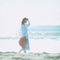 花束を持って独り海岸線を歩く青い服の女性の写真