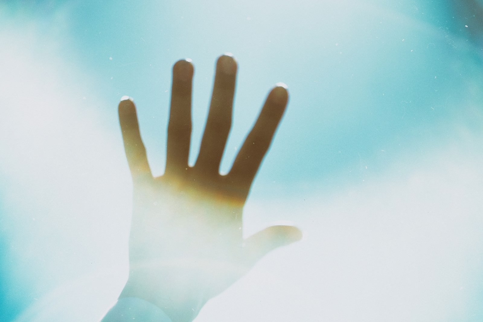 Silhouette of a hand reaching towards the bright sky