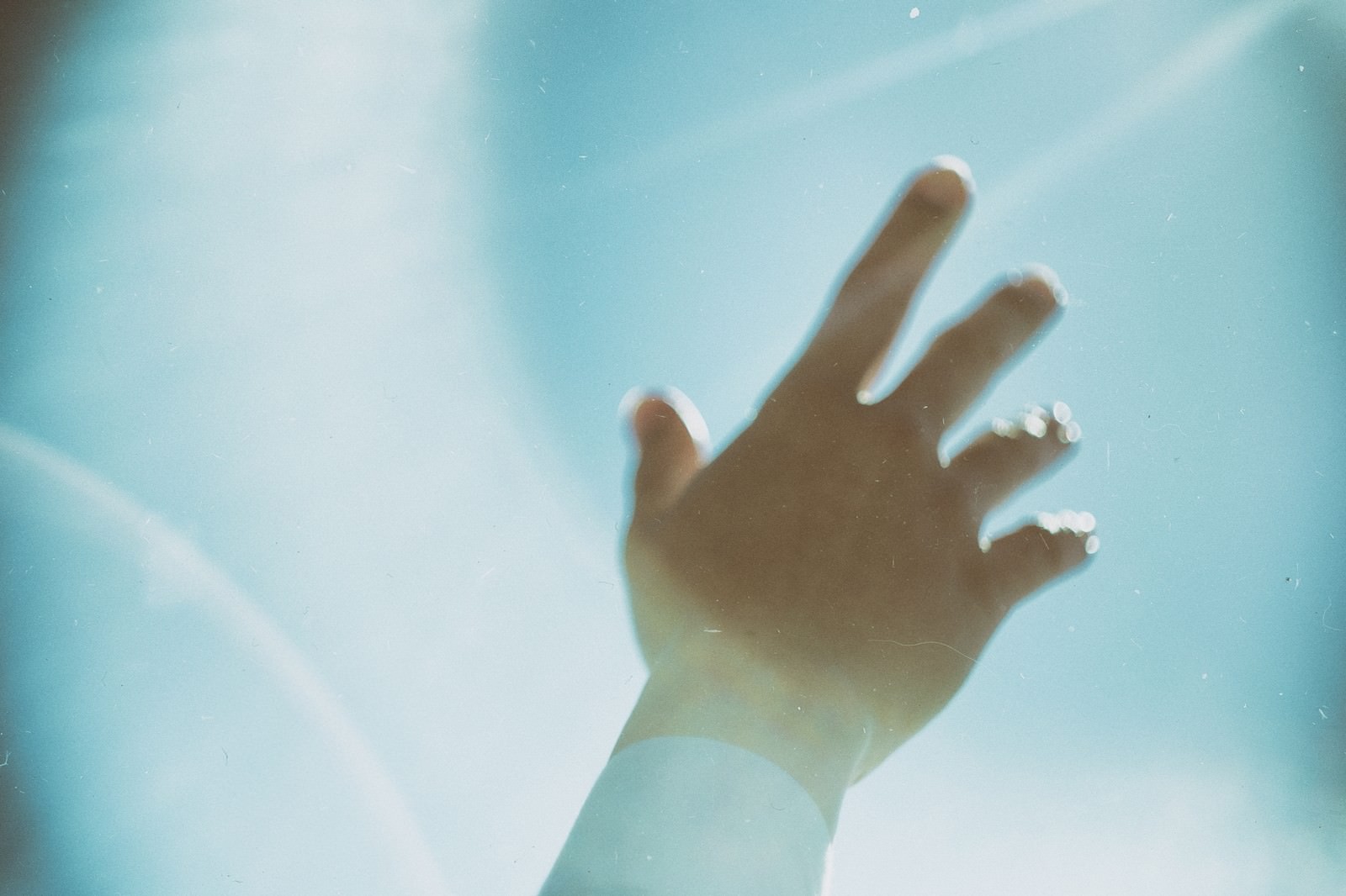 Silhouette of a hand reaching up towards the sky against a blue sky and sun