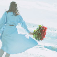 波打ち際で花束を持つ別れ寂しげな女性の後姿の写真