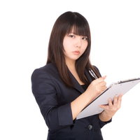 険しい表情でクリップボードにチェックを入れる人事担当の女性の写真