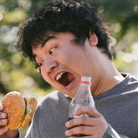 ハンバーガーとコーラを片手に食べる若い男性の昼食風景の写真