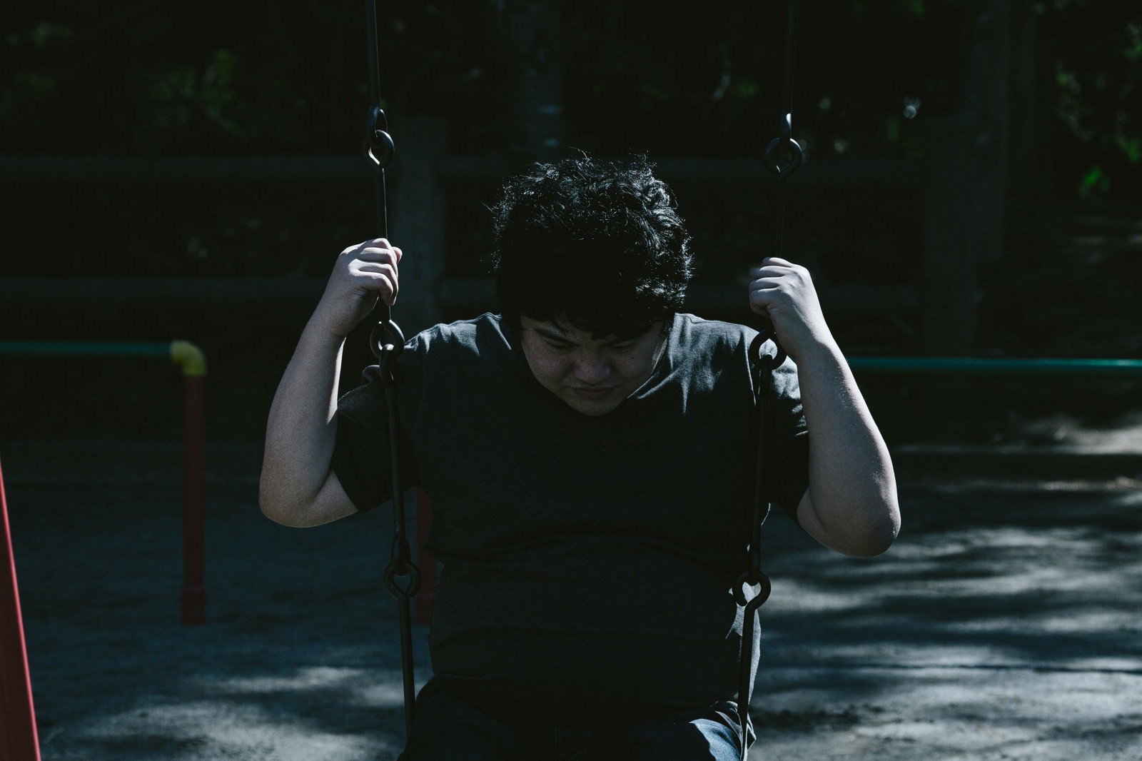 ブランコでうなだれ絶望する男性［モデル：段田隼人］