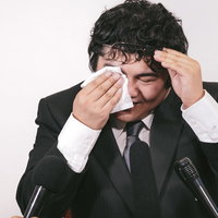 記者会見で涙を流しながら謝罪する男性ビジネスマンの写真