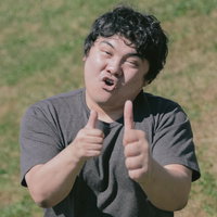 緑の芝生で両手のサムズアップポーズをする笑顔の男性の写真