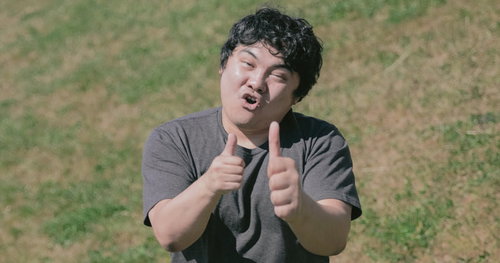 緑の芝生で両手のサムズアップポーズをする笑顔の男性