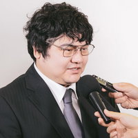 報道陣に囲まれインタビューを受けるスーツ姿の男性の写真