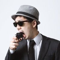 黒いスーツにサングラスで無線機を口元に持つエージェント風男性の写真