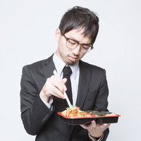 弁当を箸で食べるストライプスーツの眼鏡の会社員の写真