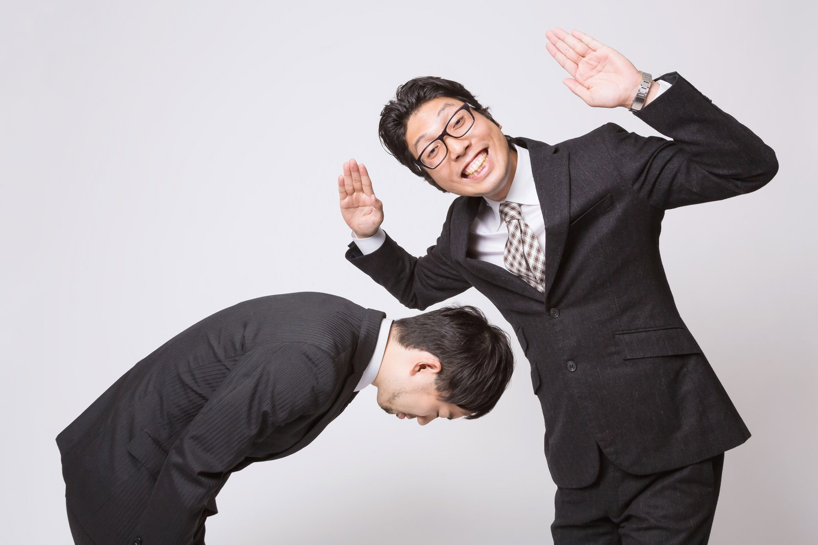 謝罪するビジネスマンと勝ち誇る男性［モデル：ひろゆき  紳さん］