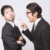 腕を組む部下と指を立てて叱る上司の写真