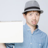 白いスケッチブックを見せるハット姿の男性の写真