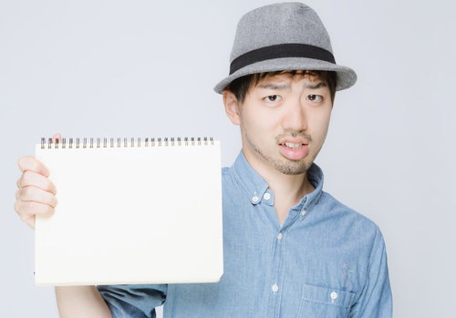 白いスケッチブックを見せるハット姿の男性