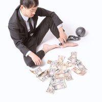 鉄球と鎖に繋がれた散らばる紙幣とスーツの男性の写真