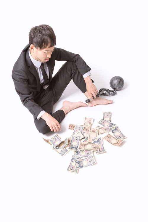 鉄球と鎖に繋がれた散らばる紙幣とスーツの男性