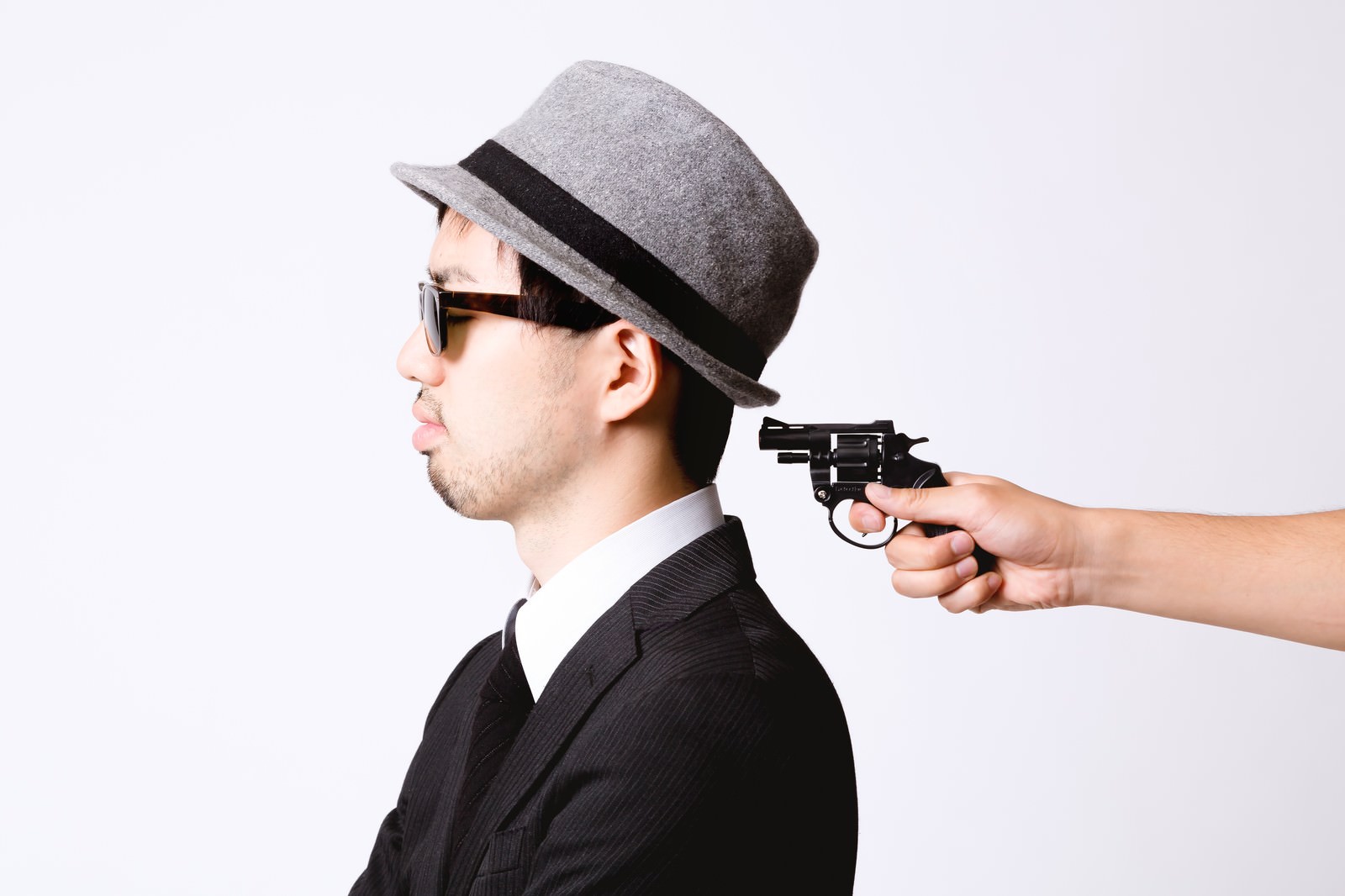 背後から拳銃を突きつけられる帽子のエージェント［モデル：ひろゆき］