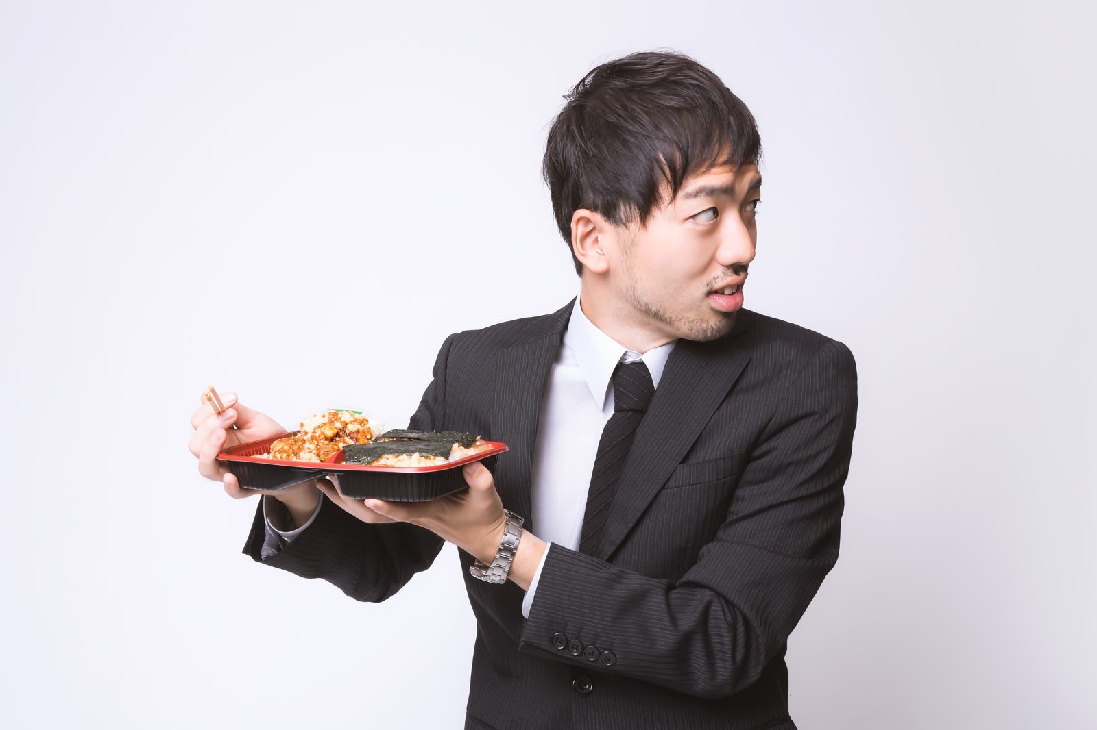 から揚げ弁当を箸で食べるスーツのサラリーマン［モデル：ひろゆき］