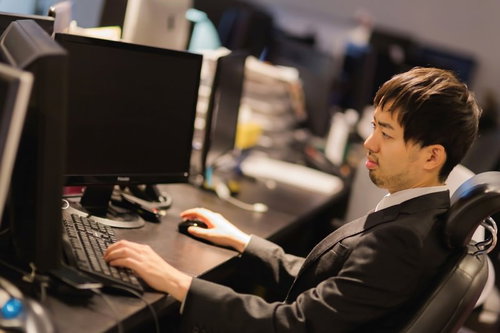 オフィスでデュアルモニターを操作するスーツの男性