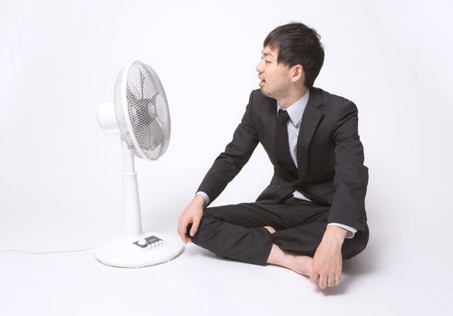 扇風機の前で涼むスーツ姿のサラリーマン