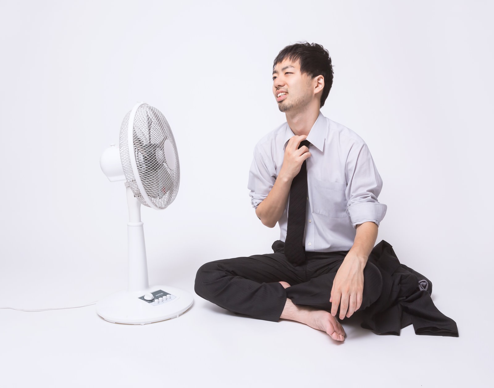 上着を脱いで扇風機に当たる水色シャツのサラリーマン［モデル：ひろゆき］
