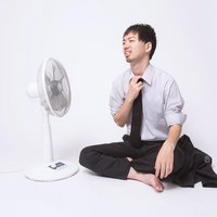 上着を脱いで扇風機に当たるサラリーマンの写真
